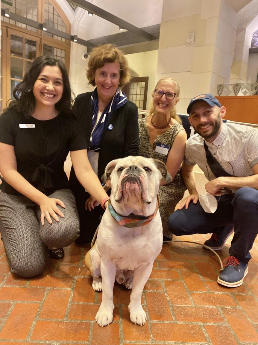 Four alumni kneeling in a half-circle around Handsome Dan, a bulldog