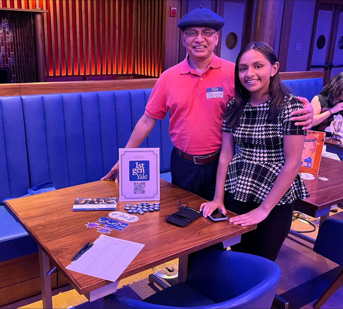 A man and a woman standing at a table with 1stGenYale info and a sign-up sheet