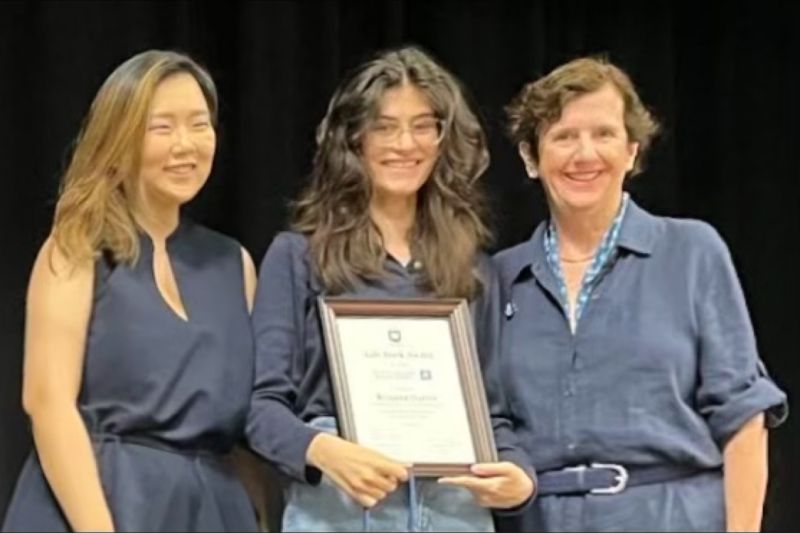 Three women stand while holding award plaque