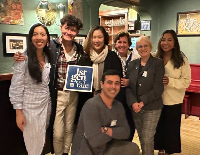 Seven alums face the camera and hold a 1stGenYale sign