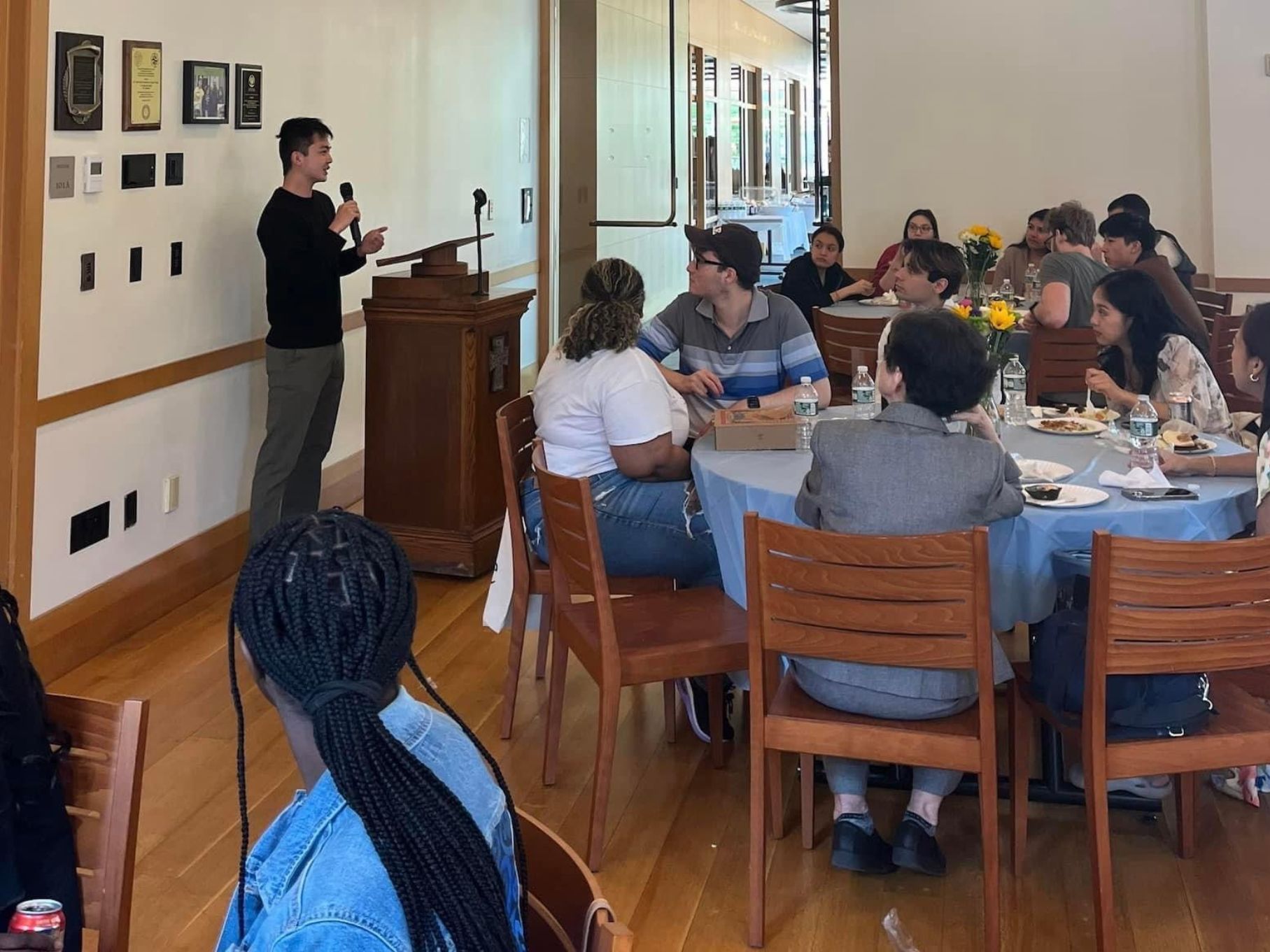 A man stands and talks at the front of the room while students sit at tables and listen